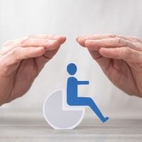 disability 1 - fundsforNGOs Two hands shielding a blue wheelchair icon, conveying accessibility protection.