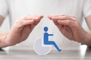 Two hands shielding a blue wheelchair icon, conveying accessibility protection.