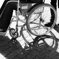 disability 2 - fundsforNGOs Person in a wheelchair being pushed on a sunlit brick sidewalk; strong shadows on the ground.
