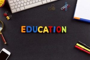 Colorful letters spelling EDUCATION on a dark desk with keyboard, notebook, paperclips, and markers nearby