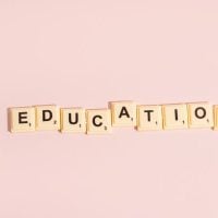 education - fundsforNGOs Wooden letter blocks spelling 'EDUCATION' on a pale pink background.