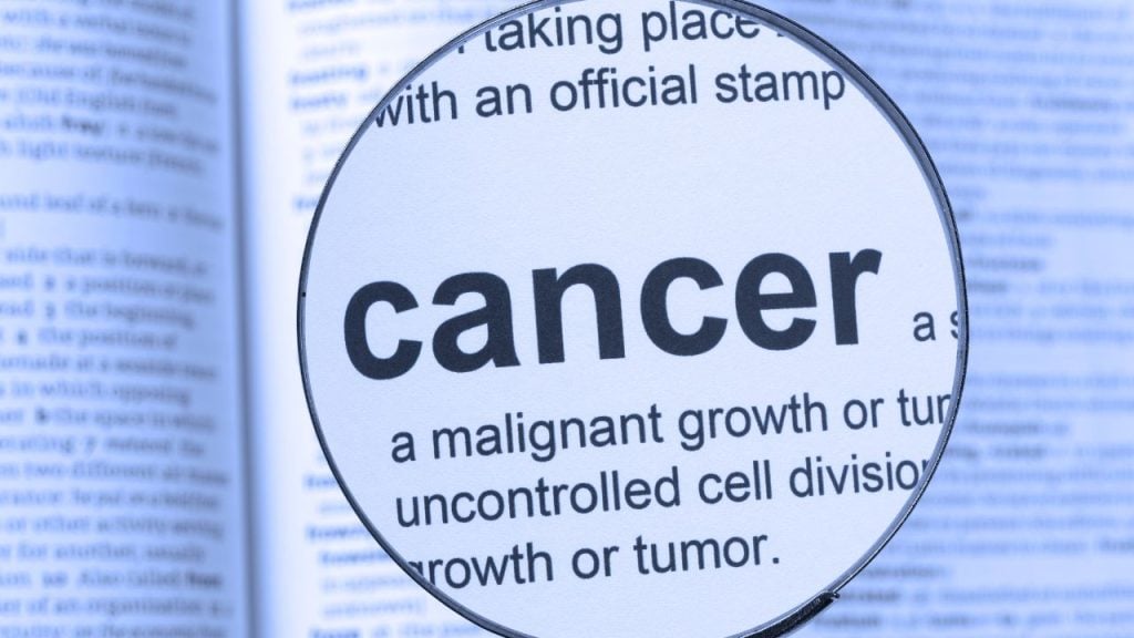 education and sports for children 2 - fundsforNGOs Magnifying glass over text reading: 'cancer' and definition 'a malignant growth or tumor' in a blue-tinted document background.