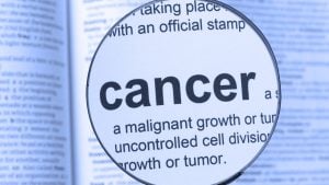 Magnifying glass over text reading: 'cancer' and definition 'a malignant growth or tumor' in a blue-tinted document background.