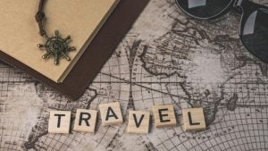 Wooden blocks spell 'TRAVEL' on a vintage map with a notebook and sunglasses nearby.