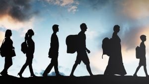 Silhouettes of five students walking in a line with backpacks against a cloudy sky at sunset/date line horizon.