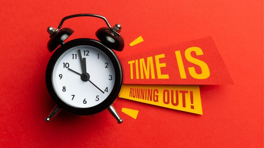Black analog alarm clock on a red surface with bold yellow banners reading 'TIME IS RUNNING OUT!'