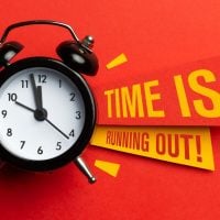 Black analog alarm clock on a red surface with bold yellow banners reading 'TIME IS RUNNING OUT!'