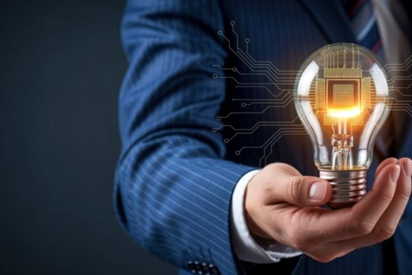 fundsforNGOs - 2026-06-01T143552105 - fundsforNGOs Businessperson in a blue suit holding a glowing light bulb with circuit patterns, symbolizing innovation and technology.