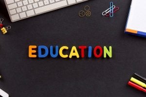 Colorful letters spelling EDUCATION on a dark desk with notebook, keyboard, and office supplies nearby (education theme).