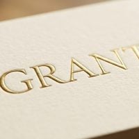 fundsforNGOs - 2026-06-01T145403329 - fundsforNGOs Close-up of a textured cream card with the word GRANT embossed in gold on the surface.