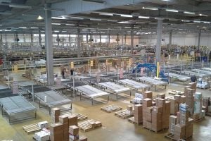 Wide view of a large warehouse with conveyor belts, tall shelves, and stacks of cardboard boxes and pallets.