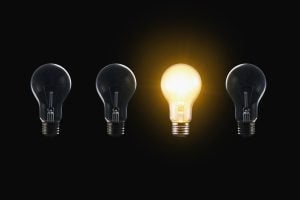 Four light bulbs in a row on a black background, with the center bulb glowing to symbolize a standout idea.