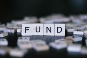 Wooden letter tiles spell 'FUND' on a dark surface with scattered tiles in the background.