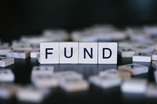 Wooden letter tiles spell 'FUND' on a dark surface with scattered tiles in the background.