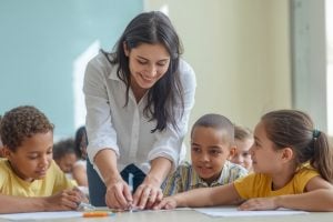 Teacher and students working together on a hands-on activity at a table in a bright classroom, pencils and papers spread out in front of them