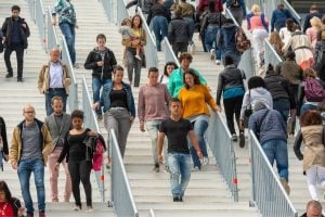 Crowd of diverse people walking up and down a wide stairway with metal railings outdoors.