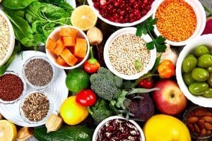 Colorful assortment of fresh vegetables, fruits, and grains in bowls and on a table. Includes leafy greens, citrus, berries, legumes, and seeds.