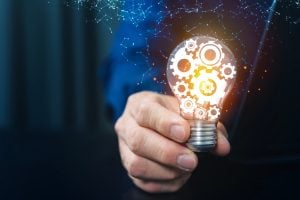 Hand holding a glowing lightbulb filled with gears, symbolizing innovation and engineering