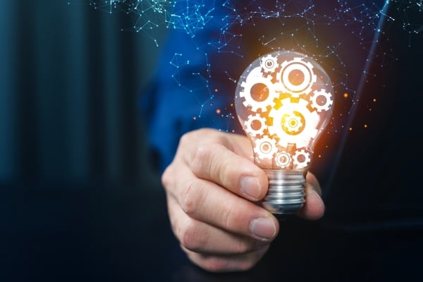 Hand holding a glowing lightbulb filled with gears, symbolizing innovation and engineering