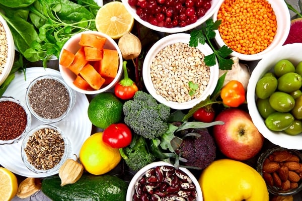Colorful assortment of fresh fruits, vegetables, legumes, and grains in bowls and on a table, highlighting healthy eating.
