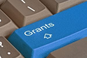 Blue keyboard key labeled 'Grants' with a cursor icon among brown keys, shown in a close-up.