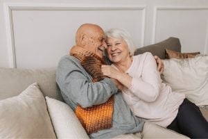 Smiling elderly couple cuddling on a sofa, sharing a warm, affectionate moment.