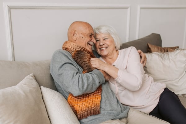 Smiling elderly couple cuddling on a sofa, sharing a warm, affectionate moment.