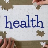 health 8 - fundsforNGOs White jigsaw puzzle with the word health in blue letters, with several hands placing pieces around it on a wooden table