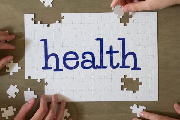 health 8 - fundsforNGOs White jigsaw puzzle with the word health in blue letters, with several hands placing pieces around it on a wooden table