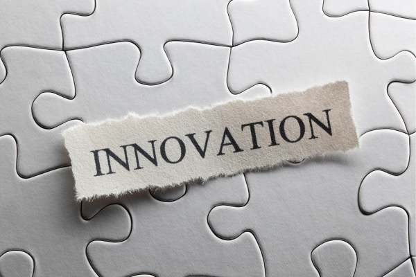 Torn paper strip with the word INNOVATION laid over a gray jigsaw puzzle background.