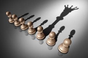 Row of brown chess pawns casting a large shadow of a reaching hand, suggesting control or manipulation.