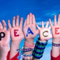 peace - fundsforNGOs Raised hands with colorful letters spelling 'PEACE' against a bright blue sky, suggesting a message of unity by kids/young people.