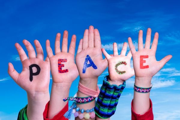 peace - fundsforNGOs Raised hands with colorful letters spelling 'PEACE' against a bright blue sky, suggesting a message of unity by kids/young people.
