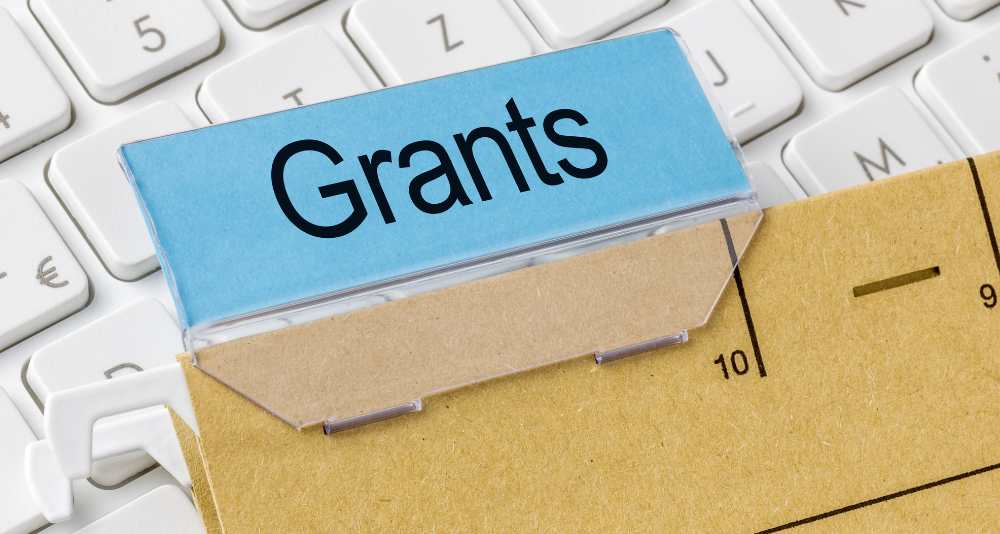 premium - 2025-09-05T113113253 - fundsforNGOs Blue card labeled 'Grants' resting on a ruler over a white keyboard, symbolizing grant funding and measurement