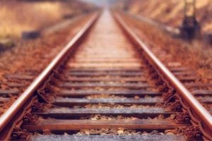 Railroad tracks stretch into the distance through an autumn landscape with fallen leaves on and between the rails.