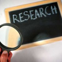 research 8 - fundsforNGOs Person holds a magnifying glass up to a chalkboard that reads 'RESEARCH'.