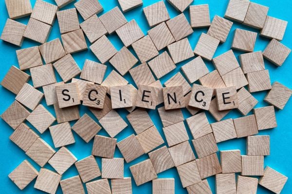 Wooden letter blocks arranged to spell 'SCIENCE' on a bright blue background, with scattered blocks around.