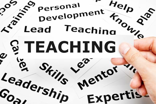 teaching - fundsforNGOs Card labeled TEACHING held by a hand, with a surrounding word cloud of leadership and education terms (lead, mentoring, skills, training, personal development).