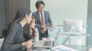 Team of three in a modern office review charts on a laptop as a presenter explains documents to them.