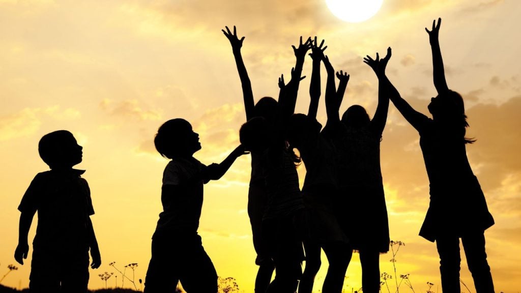education and sports for children - fundsforNGOs Silhouettes of children jumping and cheering against a golden sunset sky in a field.