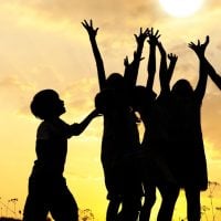education and sports for children - fundsforNGOs Silhouettes of children jumping and cheering against a golden sunset sky in a field.