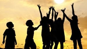 Silhouettes of children jumping and cheering against a golden sunset sky in a field.