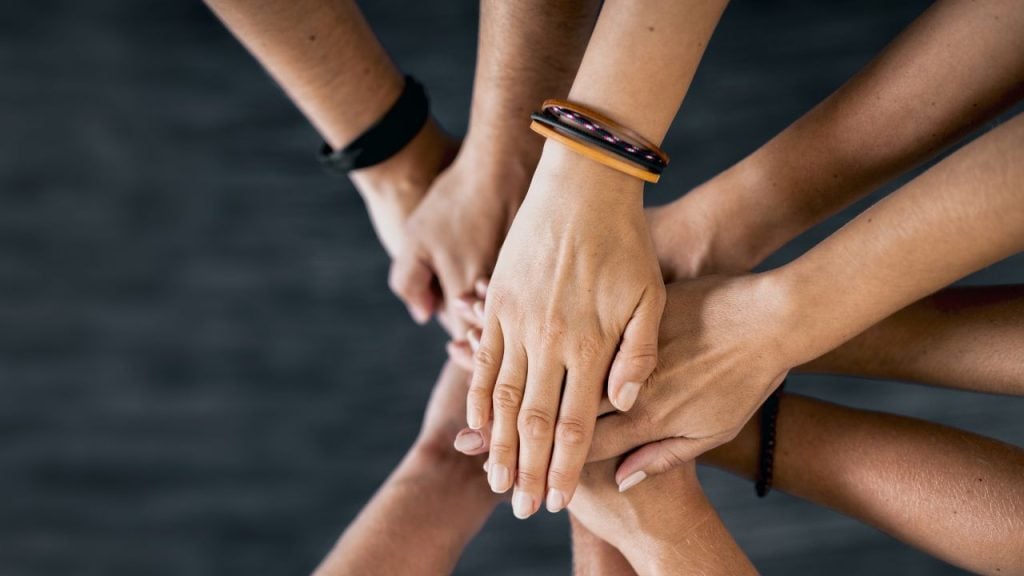 education and sports for children - fundsforNGOs Multiple hands layered together in a circle, symbolizing teamwork and unity.