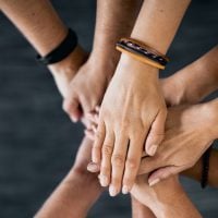 education and sports for children - fundsforNGOs Multiple hands layered together in a circle, symbolizing teamwork and unity.